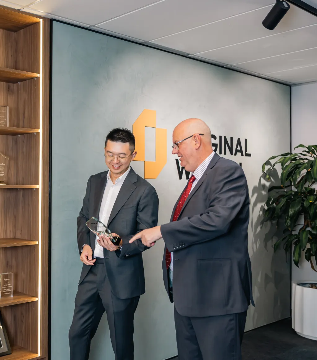 Two businessmen in suits discussing a trophy in office lobby